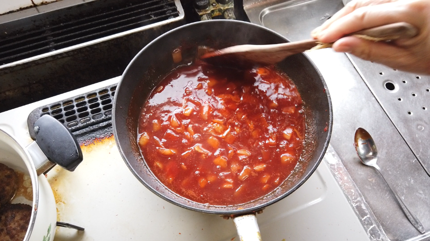 【煮込みハンバーグレシピ】６．玉ねぎを1cm角に切り、耐熱ボウルに入れ、ラップをせずに500Wの電子レンジで3分加熱します。フライパンにバターを入れて玉ねぎを炒めます。焼き色がついたら、ケチャップを入れて焼き付けます。ケチャップが渋く深い色になったら、赤ワインと塩を加え、煮立たせたら、煮込み用の鍋に加えます。