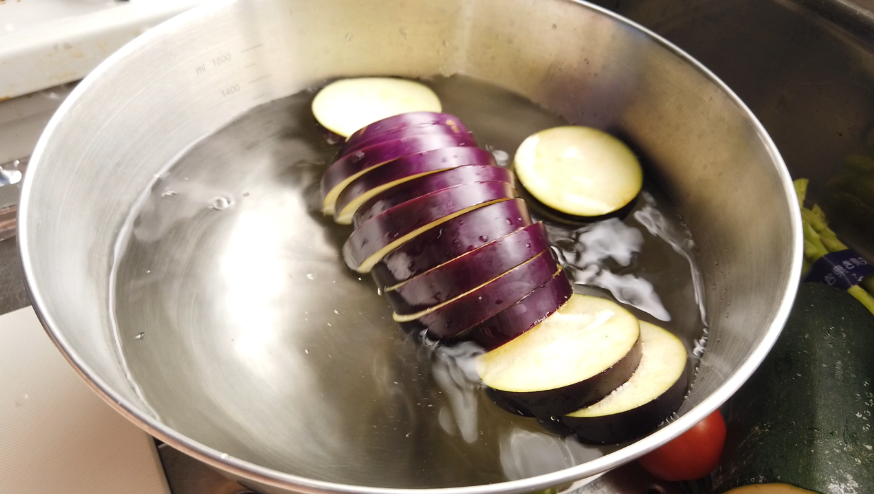 【夏野菜の揚げびたしレシピ】１．なすのヘタを落とし、輪切りにして水にさらします。ズッキーニを輪切りにします。パプリカを半分に切り、種をとって縦4等分にします。かぼちゃは種とわたを取り約5mm厚さにスライスします。ししとうを半分に切りタネを出します。オクラを斜めに切ります。アスパラガスを3等分に切ります。野菜は水気をよく拭いておきます。
