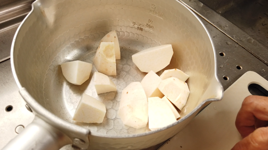【筑前煮の作り方】２．下ごしらえ。里芋の皮をむきます。里芋の皮をむく時のポイントは洗わずに厚剥きするのが手がかゆくならずに滑らないで安全に切る方法です。里芋の皮をむいたら、ひと口大に切り、水から茹でて4分ほど下ゆでをします。下茹ですることで他の食材と一緒に煮込む時間を揃えます。