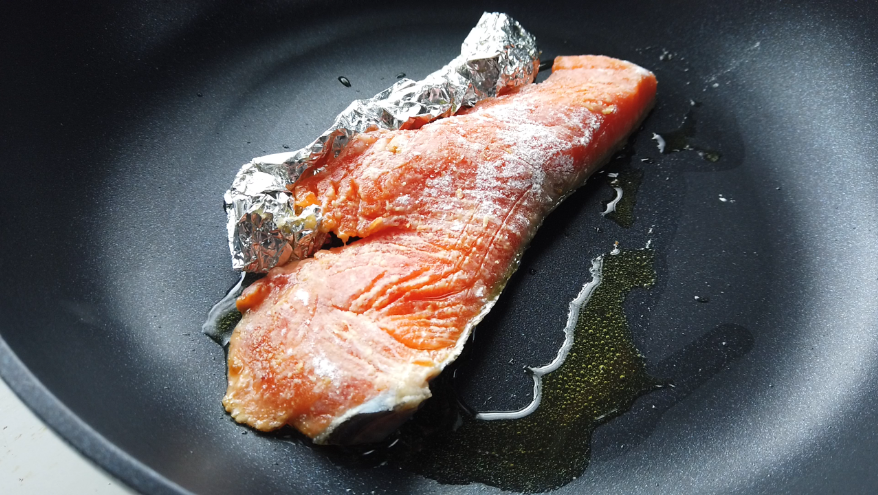 【サーモンムニエルとほうれん草のクリームソースレシピ2-1】２．フライパンにオリーブオイルをしき、フライパンが冷たい状態からオリーブオイルと鮭を入れて弱火で焼きます。まずは鮭の身の部分にくしゃくしゃにしたアルミホイルを支えにして皮目だけを焼きます。鮭から脂が出てきたらキッチンペーパーで拭きとります。皮目が焼けたら、身の片面を焼きます。